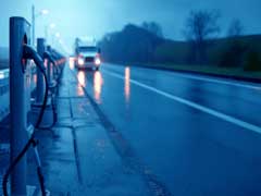 semi truck driving down a wet road on a gray day past vehicle charging stations