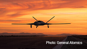A drone flies low over terrain. Photo by General Atomics.