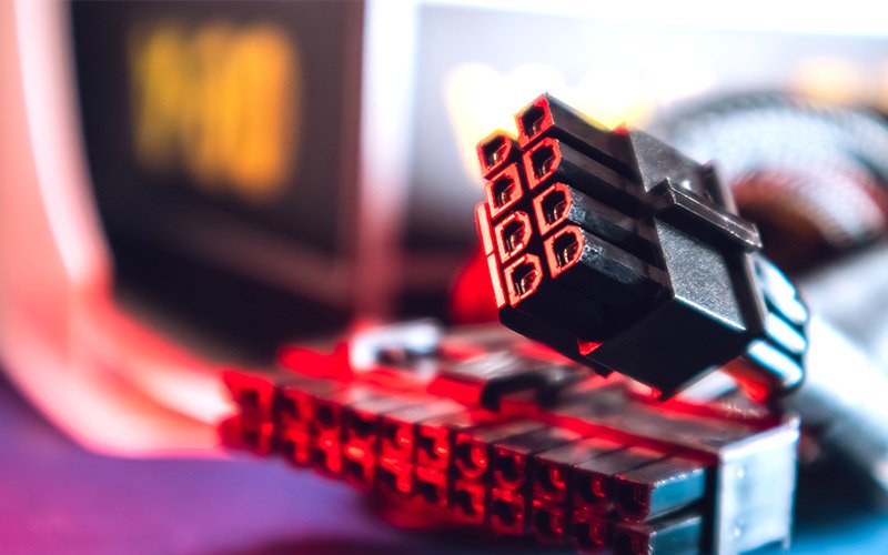 A close-up of a black computer power connector is illuminated by a red glow