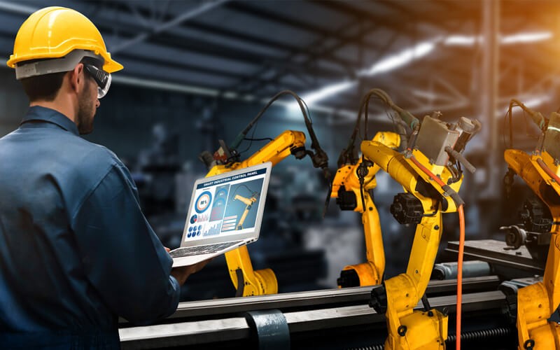 man with a laptop in front of a manufacturing robot