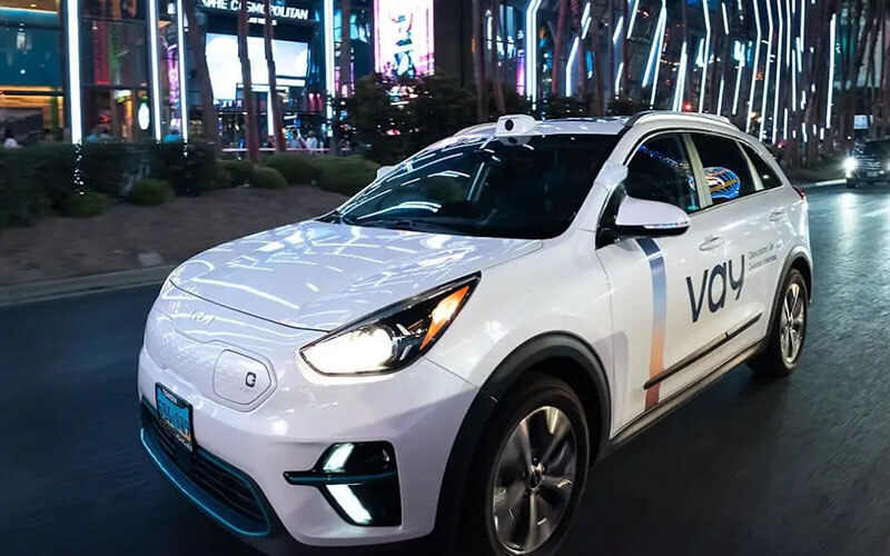 White self-driving car with roof sensors driving at night in a city.