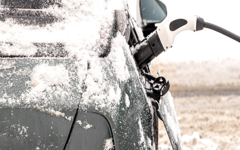A snow-covered vehicle is being cleared with an electric snow brush in a wintry landscape.