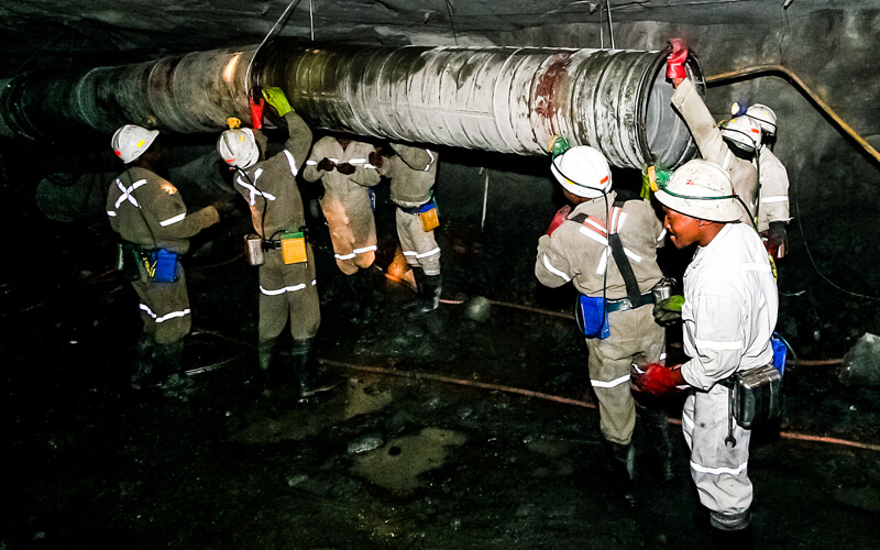 Eight people working with a large, industrial pipe