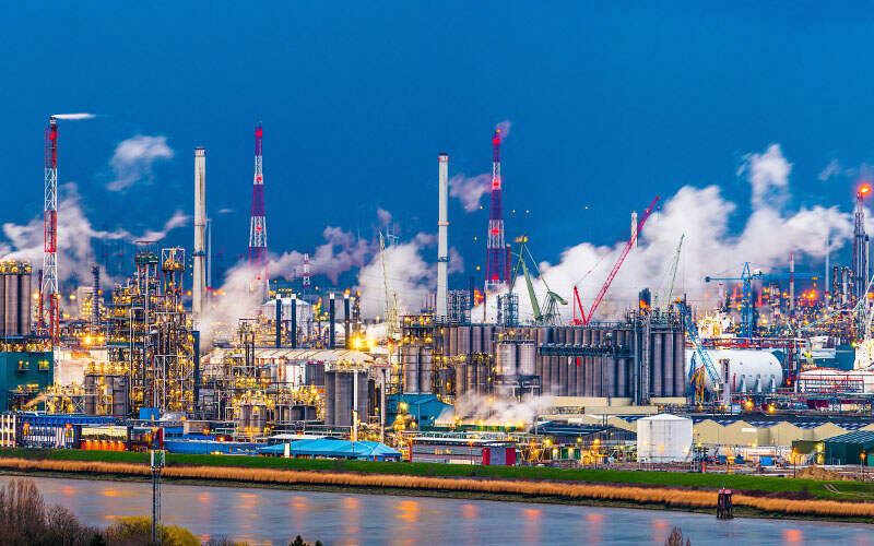 Large industrial refinery with smokestacks and storage tanks at dusk.