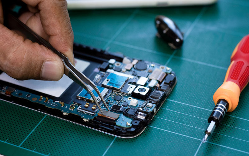 A technician repairs a smartphone using precision tools.