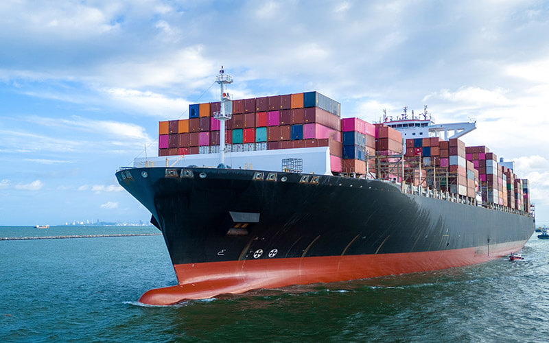 Image showing a large cargo ship loaded with colorful shipping containers moves through the water