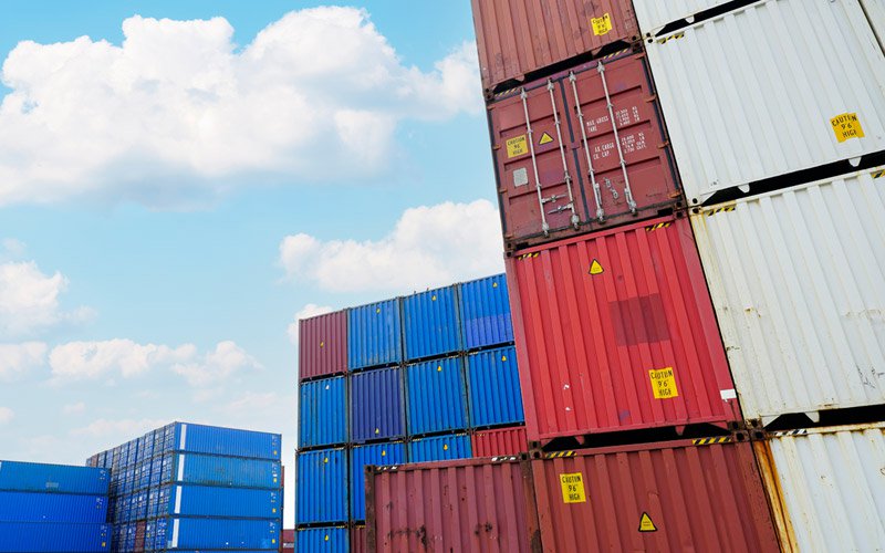 Stacked blue and red shipping containers stand tall against a blue sky.