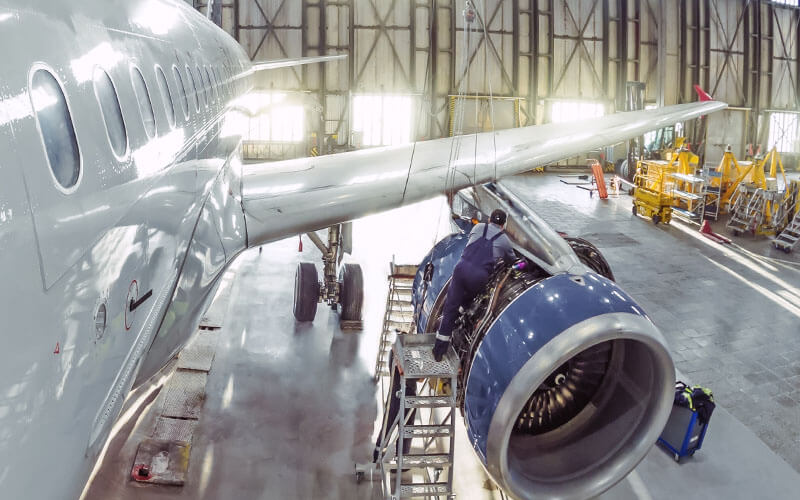 Technician performing maintenance on an aircraft engine inside a hangar.