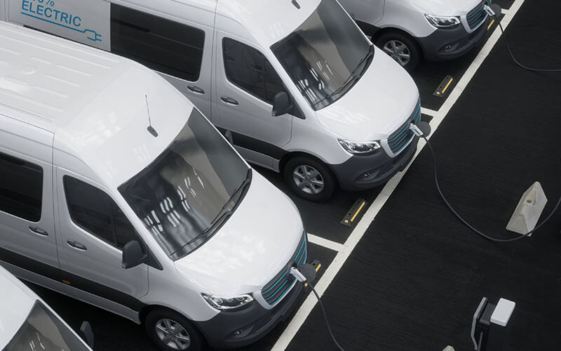 White Electric Vans Lined Up and Charging at Stations